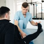 Fizjoterapeuta pomaga pacjentowi w ćwiczeniach kończyny dolnej w gabinecie