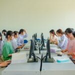 Studenci AWF pracują w grupie przy komputerach na zajęciach