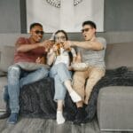Trójka przyjaciół na kanapie z piwem i popcornem podczas seansu filmowego