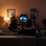 Trzy osoby na kanapie podczas wieczornego seansu filmowego w domowym salonie