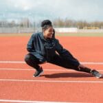 Kobieta w stroju sportowym wykonuje stretching na czerwonej bieżni