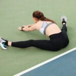 Kobieta w stroju sportowym wykonuje stretching na korcie tenisowym