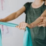 Ortopeda wspiera bark pacjentki ćwiczącej z gumą oporową