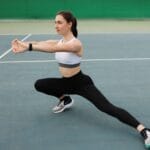 Zawodniczka rozciąga się na otwartym korcie tenisowym przed treningiem