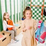 Dzieci z plecakami w kolorowej szatni, uśmiechają się i rozmawiają