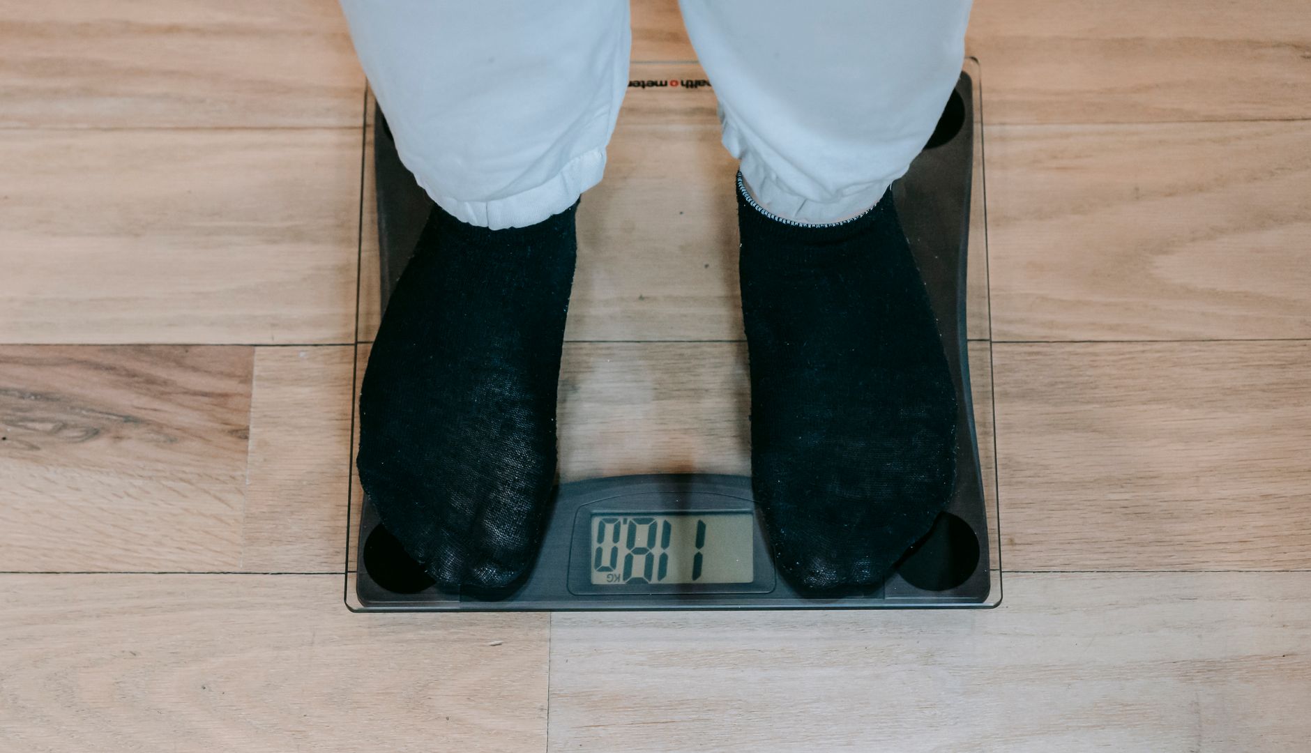 Osoba plus size stojąca na wadze łazienkowej na drewnianej podłodze